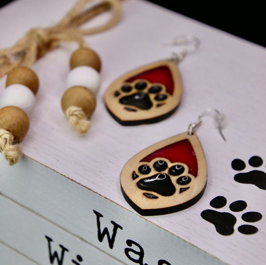 Tear drop dangle earring with a single paw print with pink and black resin, approximately 2.5 inches. They are laser cut, lightweight birchwood dangle earring that can be worn easily all day. Great gift for mom or any pet lover.