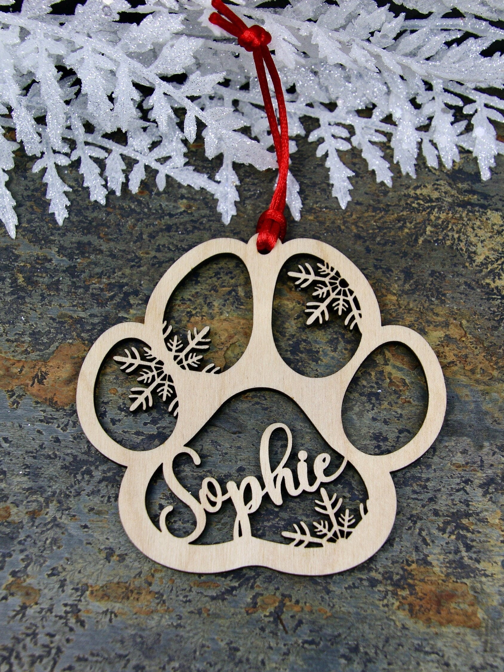 Custom wood dog paw Christmas ornament with snowflakes and personalized with your pet’s name.  

The ornaments are lightweight, laser cut, made of lightweight birchwood.